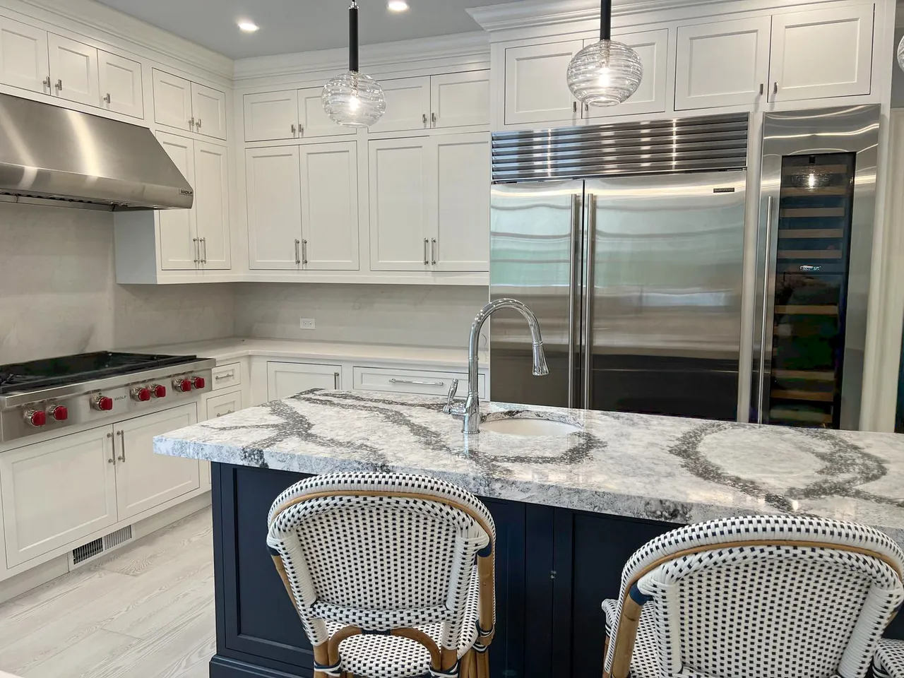 The same kitchen after renovation: painted shaker cabinets, quartz counters and a navy island