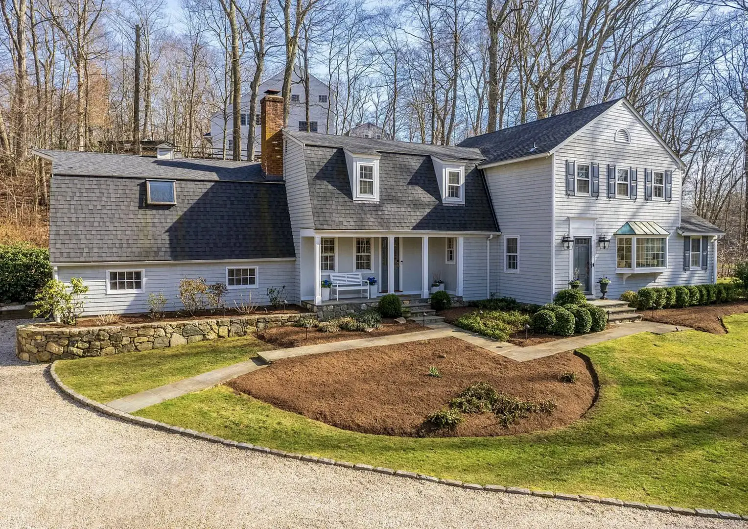 Grey-shingled colonial with a gambrel roof and a stone retaining wall