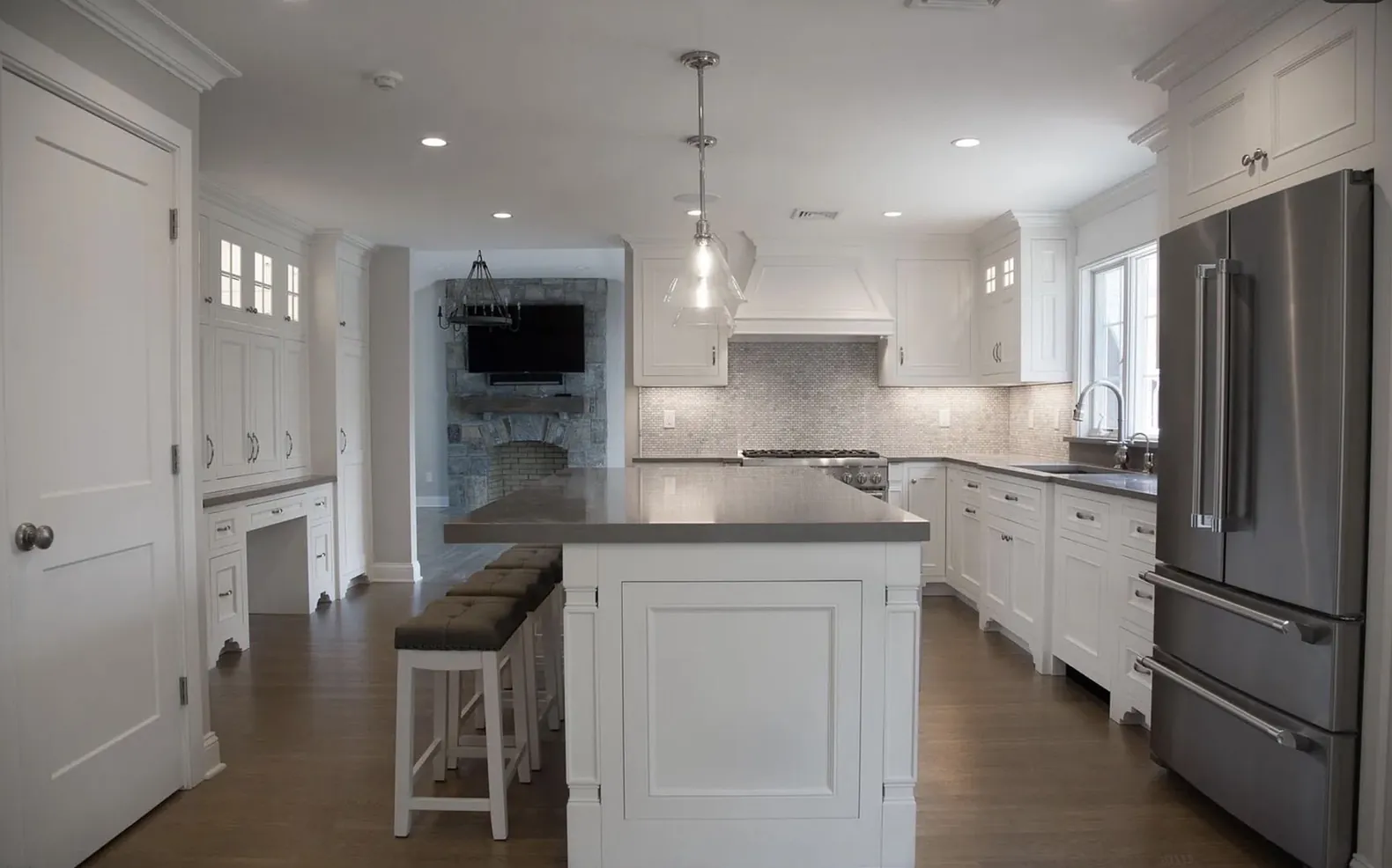 Kitchen with a long island, painted cabinetry and a stone fireplace beyond