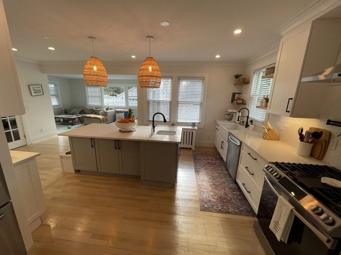Kitchen with a grey island, woven pendants and a gas range, open to the living room