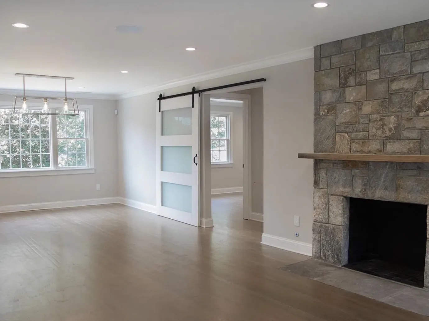 Renovated open room with a stone fireplace, a sliding barn door and refinished hardwood floors