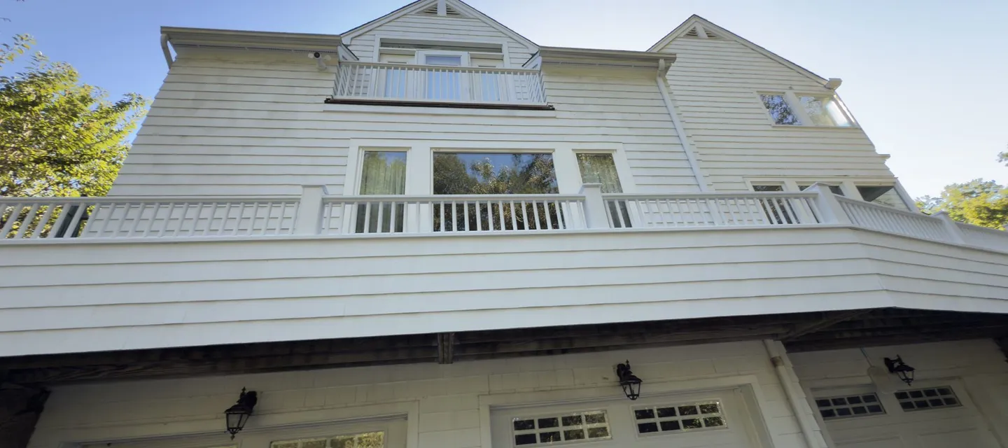 Living space and a railed deck built above a three-bay garage, with dormers and matched clapboard siding