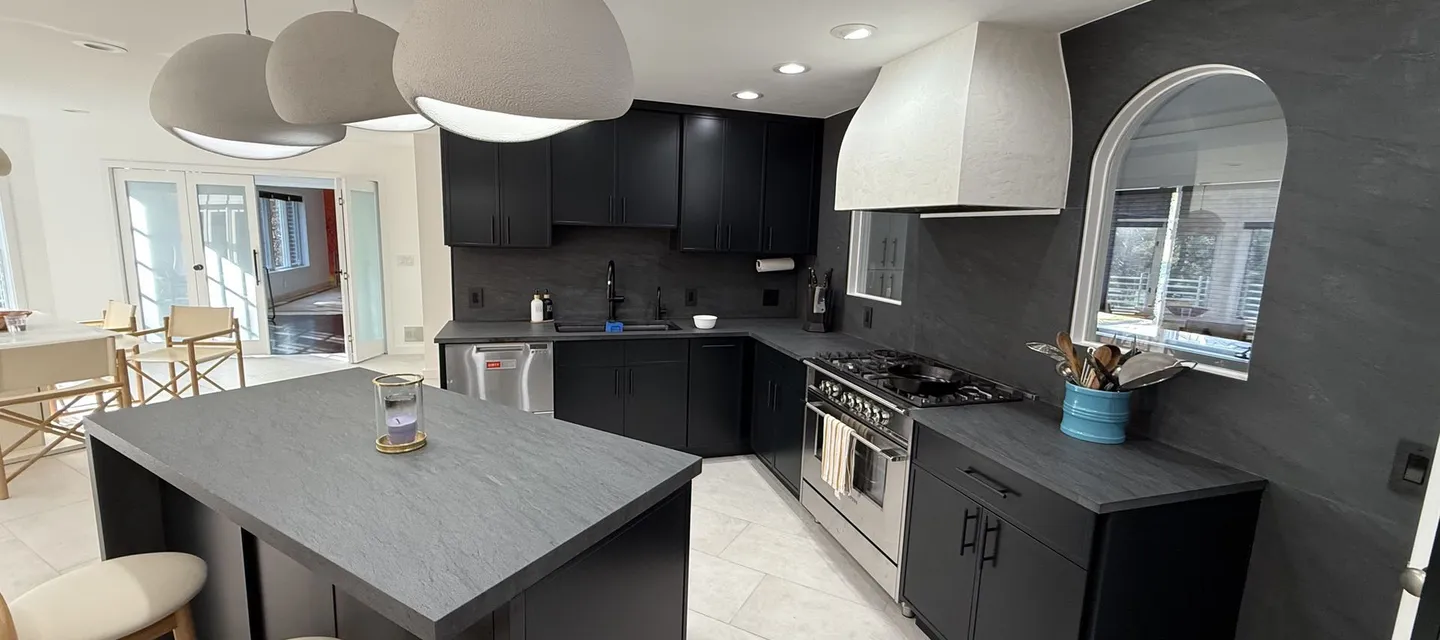 Charcoal kitchen with a white plaster range hood, arched window and a stone-topped island