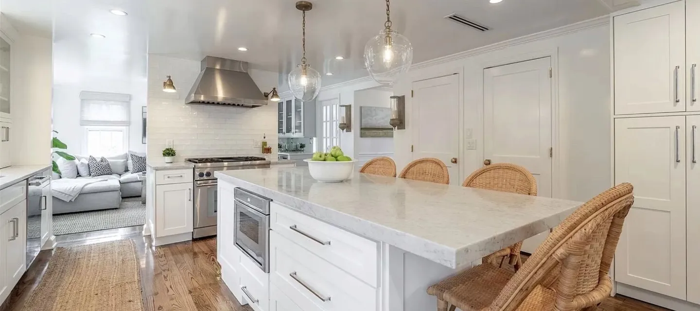 Open-plan kitchen and living room with a steel range hood, marble island and rattan stools