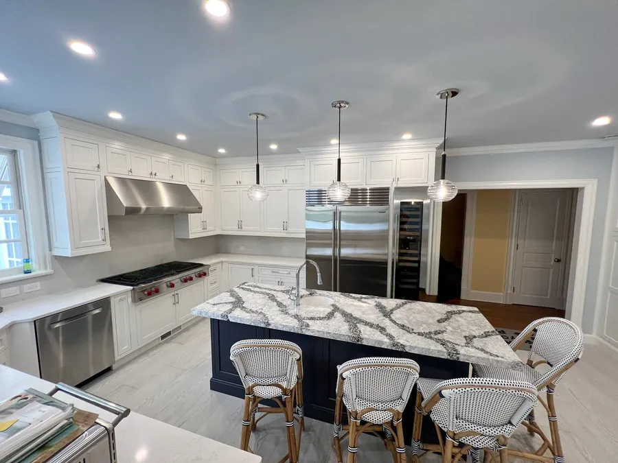 Kitchen with a navy island, marble counters and rattan bar stools